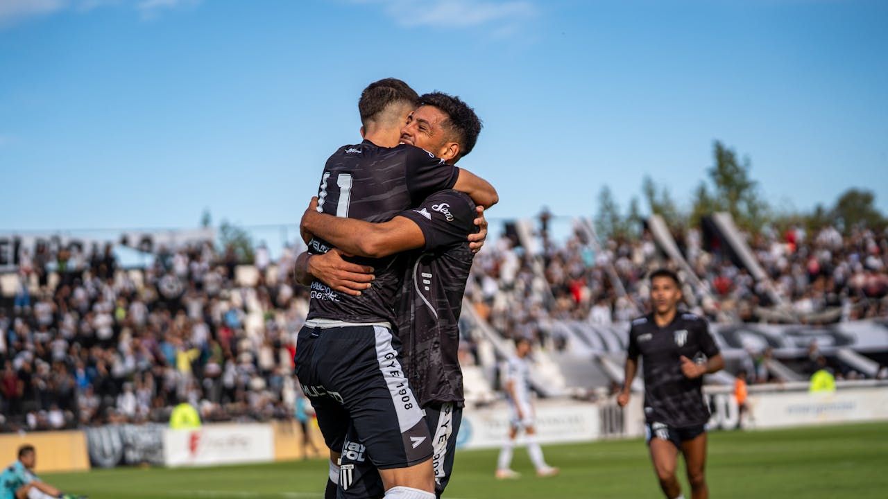Time de futebol amador comemorando vitória em campo com jogadores abraçados e torcida ao fundo